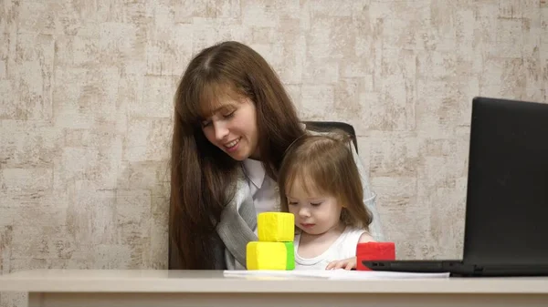 Travailler à la maison. dans la chambre, maman travaille à la table avec sa petite fille à l'ordinateur. femme d'affaires travaillant dans le bureau sur un ordinateur portable avec un bébé dans les bras. Travail indépendant féminin . — Photo