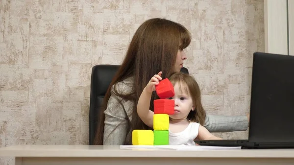 在家工作。在房间里，妈妈和她的小女儿在电脑前一起工作。在办公室工作的女商人怀里抱着一个婴儿，坐在笔记本电脑上。女性自由职业. — 图库照片