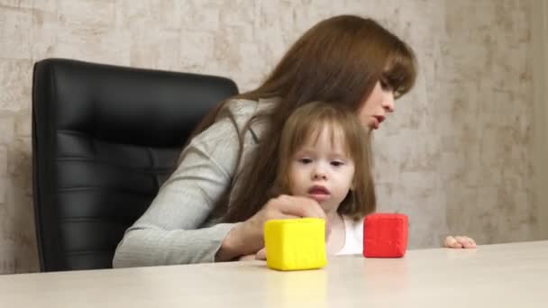 Moeder speelt met haar kind in veelkleurige kubussen op kantoor. Een drukke vrouw die werkt aan een laptop met baby op handen. Werkende moeder met mooi kind op handen in gezellig huis. jeugdconcept. — Stockvideo