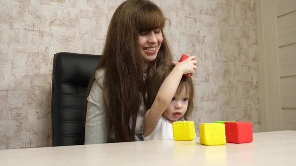 Woman works at home with a child. quarantine coronavirus. mother plays with her child in multi-colored cubes at work in office. A busy woman is working and resting with a baby in her arms. — Stock Photo, Image