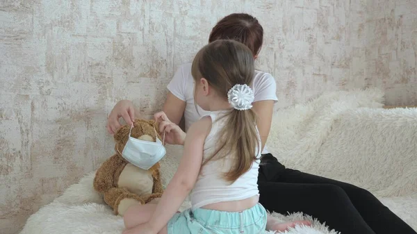 Cute baby girl quarantined, puts a medical mask on toy bear. baby plays in hospital. game pretend to be doctor nurse, veterinarian, treats an imaginary patient. teamwork of children. home games. — Stock Photo, Image