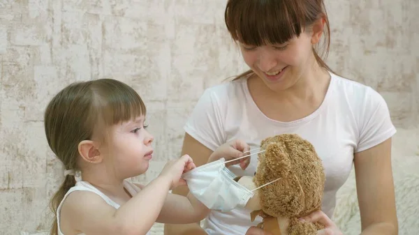 Little child girl quarantine, puts a medical mask on toy bear. protection against coronavirus and influenza. baby plays in hospital. game pretend to be doctor nurse, veterinarian, treats an patient. — Stock Photo, Image