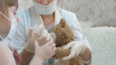 Sevimli kız oyuncak ayıya iğne yapıyor. Bebek tıbbi bir maskeyle oynuyor. Çocuk hastanede oynuyor. Oyun doktor, hemşire, veteriner gibi davranır. Aşısı olan bir hastayı iyileştirir. Koronavirüs tehlikesi