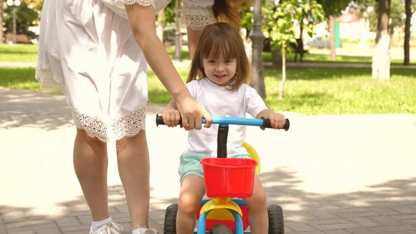 Glückliche Mutter bringt ihrer kleinen Tochter das Fahrradfahren bei. Mutter spielt mit Kind im Freien. Kind lernt Fahrradfahren. Konzept einer glücklichen Familie und Kindheit. Eltern und kleine Tochter spazieren im Park. — Stockfoto