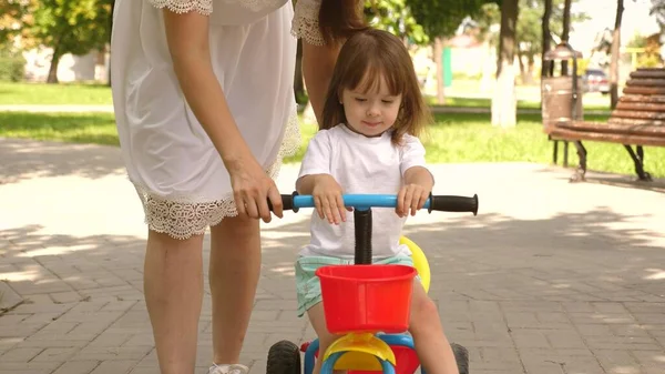 Happy mom teaches little daughter to ride a bike. mother is playing with child outdoors. child learns to ride bicycle. concept of happy family and childhood. parents and little daughter walks in park.