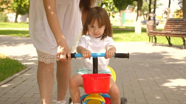 Gelukkige moeder leert kleine dochter fietsen. Moeder speelt buiten met kind. kind leert fietsen. concept van gelukkig gezin en jeugd. ouders en dochtertje wandelen in park. — Stockfoto