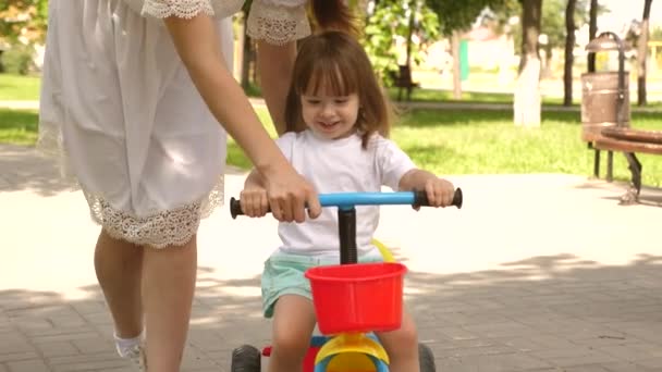 Mamá feliz enseña a su hijita a andar en bicicleta. madre está jugando con el niño al aire libre. niño aprende a andar en bicicleta. concepto de familia feliz y la infancia. padres y pequeña hija camina en el parque . — Vídeo de stock