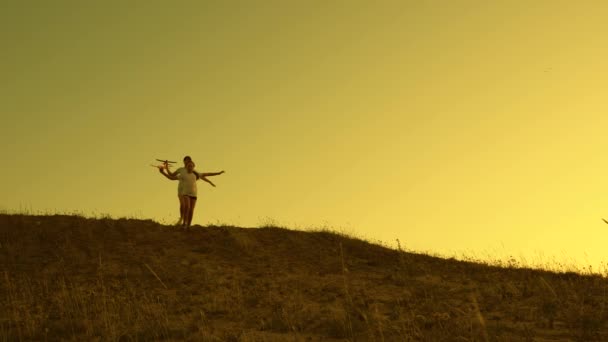 Mädchen spielen bei Sonnenuntergang mit einem Spielzeugflugzeug. Kinder laufen mit dem Flugzeug in der Hand vor der Sonne vom Berg. Träume vom Fliegen. Glückliche Kindheit. Silhouette von Kindern, die im Flugzeug spielen — Stockvideo