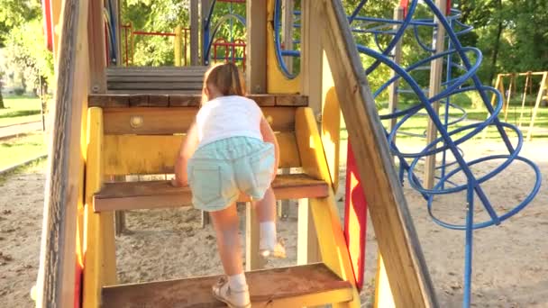 Concepto de infancia feliz. niño sube las escaleras hasta el tobogán de niños. madre y bebé juegan en el patio de recreo. feliz infancia y concepto familiar. niño se ríe y disfruta de parque infantil en el parque — Vídeo de stock