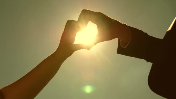 Fare una forma di cuore con le dita, un simbolo di amore e vita. sole in mano. Silhouette di coppia amorevole rendendo il simbolo del cuore con le mani di fronte al sole all'orizzonte. lavoro di squadra di coppia amorevole . — Video Stock