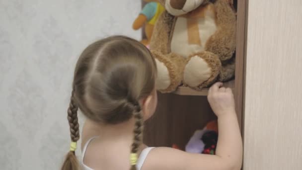 小さな幸せな女の子が積極的にぬいぐるみやテディベアと遊ぶ。子供は子供部屋で遊んでいます。子供はおもちゃを遊ぶのが好きだ。子供と家族の概念は — ストック動画