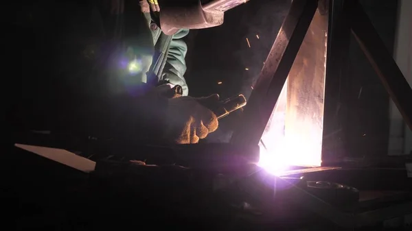 Jasné světlo a jiskry ze svařování. Průmyslový pracovník v ochranné masce s využitím moderního svařovacího stroje pro svařování kovových konstrukcí v průmyslové výrobě v závodě na zpracování kovů. — Stock fotografie