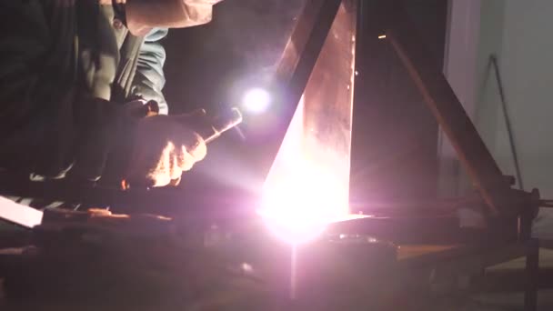Jasne światło i iskry od spawania. Pracownik przemysłowy w masce ochronnej wykorzystujący nowoczesną spawarkę do spawania konstrukcji metalowych w produkcji przemysłowej w zakładzie obróbki metali. — Wideo stockowe