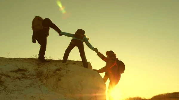 Μια ομάδα ορειβατών σκαρφαλώνει σε ένα βουνό κρατώντας ένα χέρι βοηθείας ο ένας στον άλλο. Ελεύθερη γυναίκα ταξιδιώτης αναρριχηθεί στο βουνό. ομαδική δουλειά των τουριστών. Ταξίδι και περιπέτεια στα βουνά στο ηλιοβασίλεμα. — Φωτογραφία Αρχείου