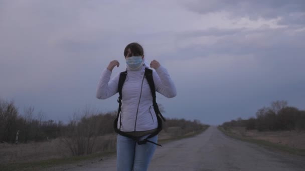 Fri jente-reisende med ryggsekk i beskyttende medisinsk maske og hette går ut av byen på vei. Beskyttelse mot virus og bakterier. helse- og sikkerhetskonsept, coronavirus N1H1, virus – stockvideo