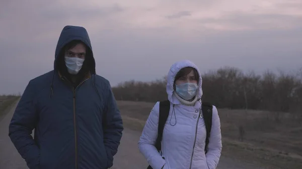 보호 마스크를 쓴 가방을 들고 도시를 탈출하는 남녀 가 도로를 따라 도시 밖을 걷고 있다. 바이러스 와 박테리아 로부터 보호 한다. 보안 개념, 코로나 바이러스 N1H1 — 스톡 사진