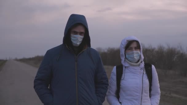 Kadın ve erkek koruyucu maske ve kapüşonlu bir sırt çantasıyla şehirden kaçıyorlar. Şehir dışında yol boyunca yürüyorlar. Virüs ve bakterilere karşı koruma. Güvenlik Konsepti, Coronavirus N1H1 — Stok video