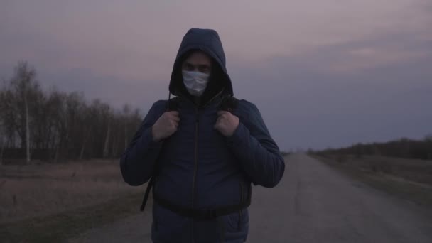 Man escaping leave city with a backpack in protective medical mask and hood are walking outside city along road. Protection against viruses and bacteria. Security Concept, Coronavirus N1H1 — Stock Video
