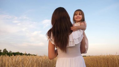 Mutlu aile yolculukları. Annenin kollarında bir bebek. Mutlu aile kavramı. Anne ve küçük kızı güneşte olgunlaşmış buğday tarlasında oynuyorlar. Anne buğdaylı bir tarlada bir çocukla yürüyor..