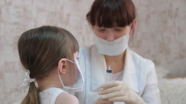 Niña sana inyecta un oso de juguete. niño juega con máscara médica. niño juega en el hospital. juego pretende ser un médico, enfermera, veterinario, trata a un paciente con una vacuna. peligro de coronavirus — Vídeo de stock