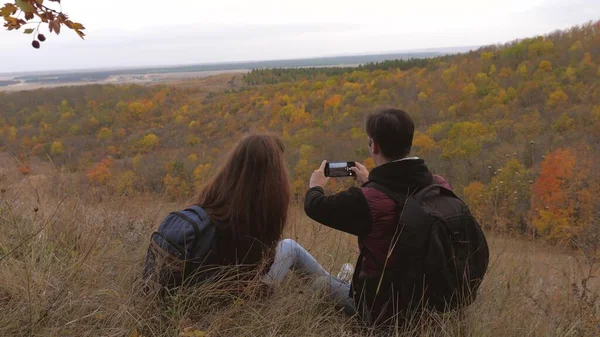 Volný muž a žena s batohy vzít selfie na horu. cestovatelé jsou fotografováni na telefonu proti krásné krajině. turisté fotit pro paměť. Týmová práce poutníků. koncept dobrodružství — Stock fotografie