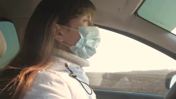 Здоровая молодая женщина в защитной стерильной медицинской маске водит машину. понятие пандемического коронавируса. свободная девушка путешествует в маске в машине. защита от вирусов и бактерий. девушка ездит на машине — стоковое видео