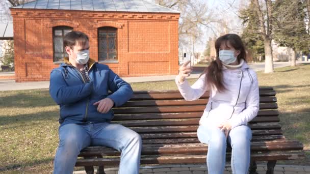 Skydd mot Coronavirus. kvinna och man i medicinsk skyddsmask sitter med smartphone på en stadsgata i Europa. Turister på gatan bär en skyddande mask från virus selfies på smartphone. — Stockvideo