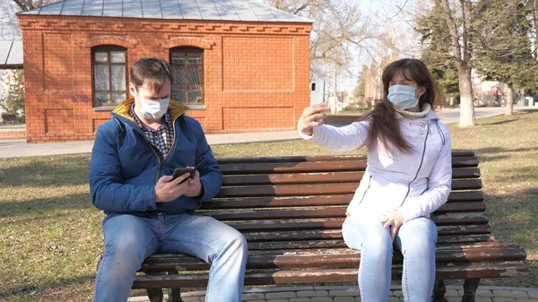 코로나 바이러스 보호. 의료용 마스크를 쓴 남녀들 이 유럽의 한 도시 거리에서 스마트폰을 들고 앉아 있습니다. 거리의 관광객들은 스마트폰에서 바이러스로부터 보호 마스크를 착용 한다. — 스톡 사진