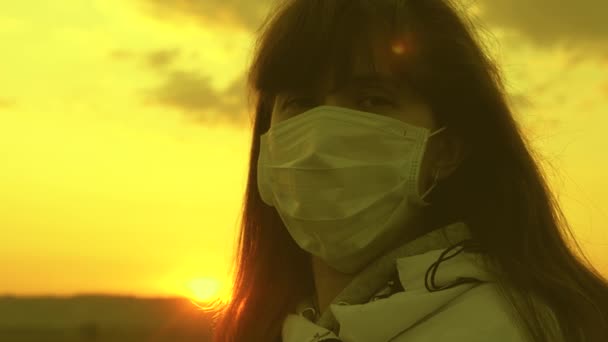 Gün batımında koruyucu bir maske takan özgür bir kadın. Yakın plan. Virüs ve bakterilere karşı koruma. Sağlık ve güvenlik konsepti, koronavirüs N1H1, virüs koruması. Pandemik koronavirüs. — Stok video