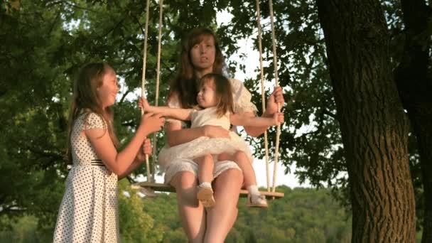 Família feliz saudável. mãe com filhos sacode uma filha bonita em um balanço em um parque em uma árvore. sonho de voar. O conceito de uma família feliz e infância. mãe e filha estão brincando no parque — Vídeo de Stock