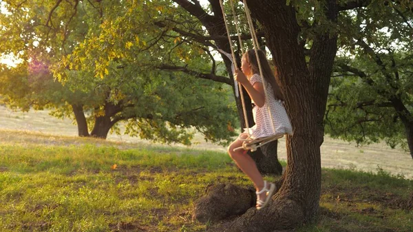 Hälsosam lycklig pojke. Flickan leker på en gunga i en park på ett träd. Dröm om att flyga. Begreppet lycklig familj och barndom. dotter spelar i parken. — Stockfoto