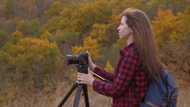Koncepcja podróży. darmowa dziewczyna podróżnik z aparatem sprawia, że piękne zdjęcia natury. niezależna kobieta fotograf turystyczny robi zdjęcia pięknego jesiennego krajobrazu z profesjonalnym aparatem cyfrowym — Wideo stockowe
