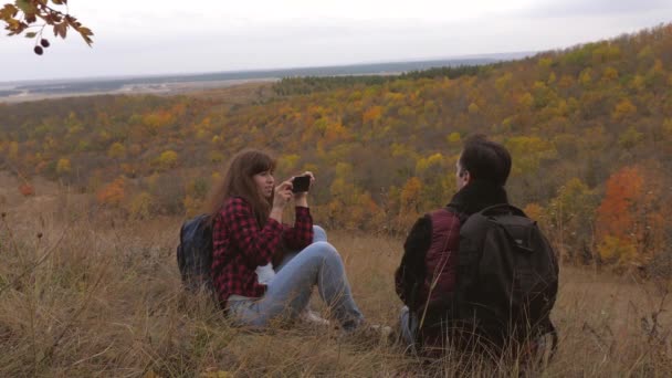 Podróżni są fotografowani na smartfonie na tle pięknego krajobrazu. turyści robią zdjęcia dla pamięci. podróżnych do pracy zespołowej. wolny mężczyzna i kobieta z plecakami robić selfie na wzgórzu — Wideo stockowe