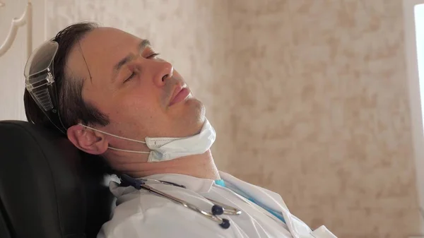 病気の治療と支援の概念です。クリニックオフィスでの睡眠男性医師は仕事に疲れている。男性の医療従事者は病院の椅子に身を包んだ。医者は疲労と過労で目を閉じて. — ストック写真