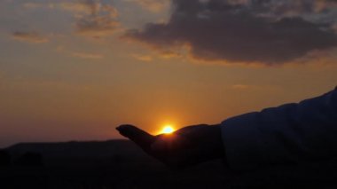 Özgür kız gezgin güneşi avuçlarında tutuyor. Sağlıklı bir kadın seyahat eder ve günbatımından hoşlanır. Güneşle el ele oynayın. Seyahat ve macera konsepti. İyi bir yarın için umut ve inanç