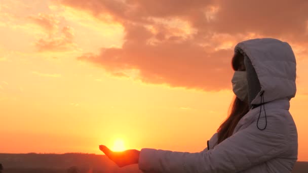 Hälso- och säkerhetskoncept, coronavirus N1H1. hopp om helande och imorgon. fri kvinna bär en skyddande medicinsk mask håller solen i händerna vid solnedgången. Skydd mot virus och bakterier. — Stockvideo