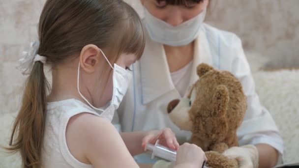 Spel doet zich voor als een arts, verpleegster, dierenarts, behandelt een patiënt met een vaccin. gevaar voor het coronavirus. gezond meisje injecteert een speelgoedbeer. kind speelt met medisch masker. kind speelt in ziekenhuis. — Stockvideo