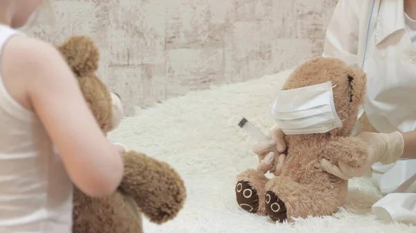 Дети играют с игрушечными медведями в медицинских защитных масках. Игра притворяется врачом, медсестрой, ветеринаром, лечит пациента вакциной. опасность коронавируса. ребенок играет в больнице . — стоковое фото