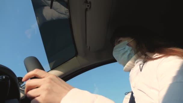 Mujer joven y saludable con máscara médica estéril protectora conduce un coche. concepto de coronavirus pandémico. chica libre viaja en una máscara en un coche. protección contra virus y bacterias. una chica monta un coche — Vídeos de Stock