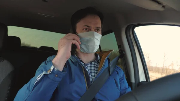 Το αγόρι οδηγεί και μιλάει στο ανδροειδές. Ένας υγιής νεαρός με αποστειρωμένη ιατρική μάσκα οδηγεί αυτοκίνητο. Ελεύθερος άνθρωπος με κινητό ταξιδεύει με μάσκα στο αυτοκίνητο. προστασία από ιούς και βακτήρια. — Φωτογραφία Αρχείου