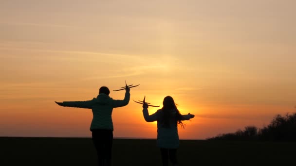 Silhouet van gezonde kinderen die in een vliegtuig spelen. Dromen van vliegen. concept van een gelukkige jeugd. Twee vrije meisjes spelen met een speelgoedvliegtuig. Kinderen op de achtergrond van de zon met een vliegtuig in zijn hand — Stockvideo