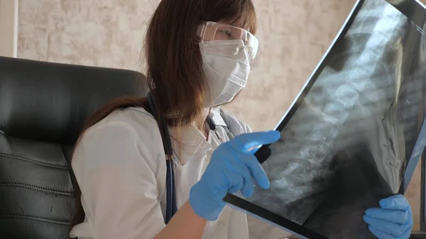 Médecin femme au bureau examine une radiographie du patient à l'hôpital. pandémie de coronavirus, pneumonie traitement COVID-19. Un médecin travaille dans un bureau d'hôpital. Soins médicaux et concept de soins de santé . — Photo