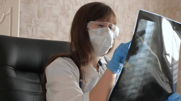 Läkarkvinnan på kontoret undersöker en röntgen av patienten på sjukhuset. behandling med coronavirus pandemi, pneumoni COVID-19. En läkare arbetar på ett sjukhus kontor. Medicinsk vård och hälsovård. — Stockfoto