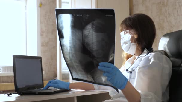 Ofisteki bir kadın doktor hastanede bir hastanın röntgenini çekiyor. Doktor hastane ofisinde dizüstü bilgisayarla çalışıyor. Tıbbi bakım ve sağlık hizmeti kavramı. Koronovirüs salgını, zatürree COVID-19. — Stok video