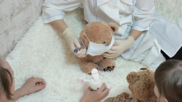Çocuklar hastanede oynuyor. Çocuklar tıbbi koruyucu maskeli oyuncak ayılarla oynarlar. Oyun doktor, hemşire, veteriner gibi davranır. Hastayı aşıyla tedavi eder. Koronavirüs tehlikesi. — Stok video