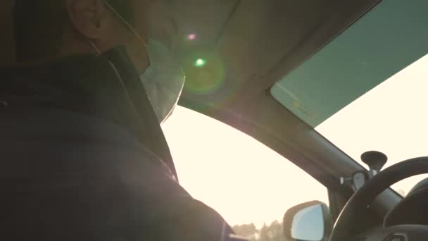 Il ragazzo sta guidando e parlando di android. Un ragazzo sano con una maschera protettiva sterile guida un'auto. Uomo libero con un telefono cellulare viaggia in maschera in auto. protezione contro virus e batteri. — Video Stock