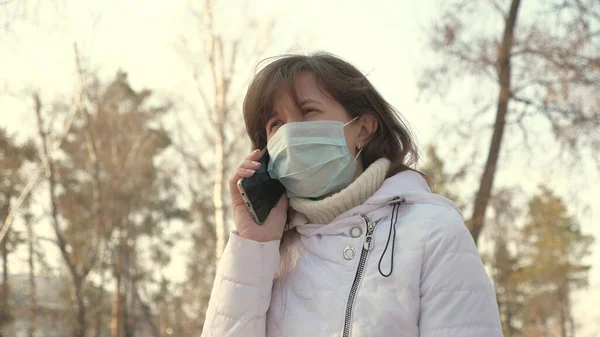 Ung kvinna i en medicinsk skyddsmask sitter med en smartphone på stadens gata i Europa. Skydd mot Coronavirus. Turister på gatan bär skyddsmask från virus. begrepp hälsa och säkerhet — Stockfoto