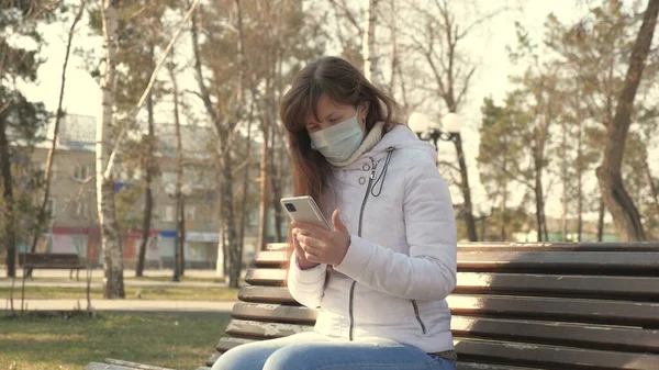 验尸官的保护。在欧洲的城市街道上，戴着医疗防护面具的年轻女性正拿着智能手机坐在那里。街上的游客戴着防毒面具。概念、健康和安全 — 图库照片