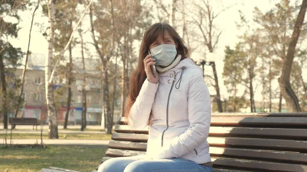 concept health and safety. young woman in a medical protective mask is sitting with a smartphone on city street in Europe. Coronavirus protection. tourists on street wear protective mask from viruses.