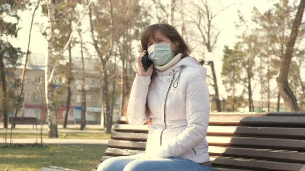 Begreppet hälsa och säkerhet. ung kvinna i en medicinsk skyddsmask sitter med en smartphone på stadens gata i Europa. Skydd mot Coronavirus. turister på gatan bära skyddsmask från virus. — Stockfoto